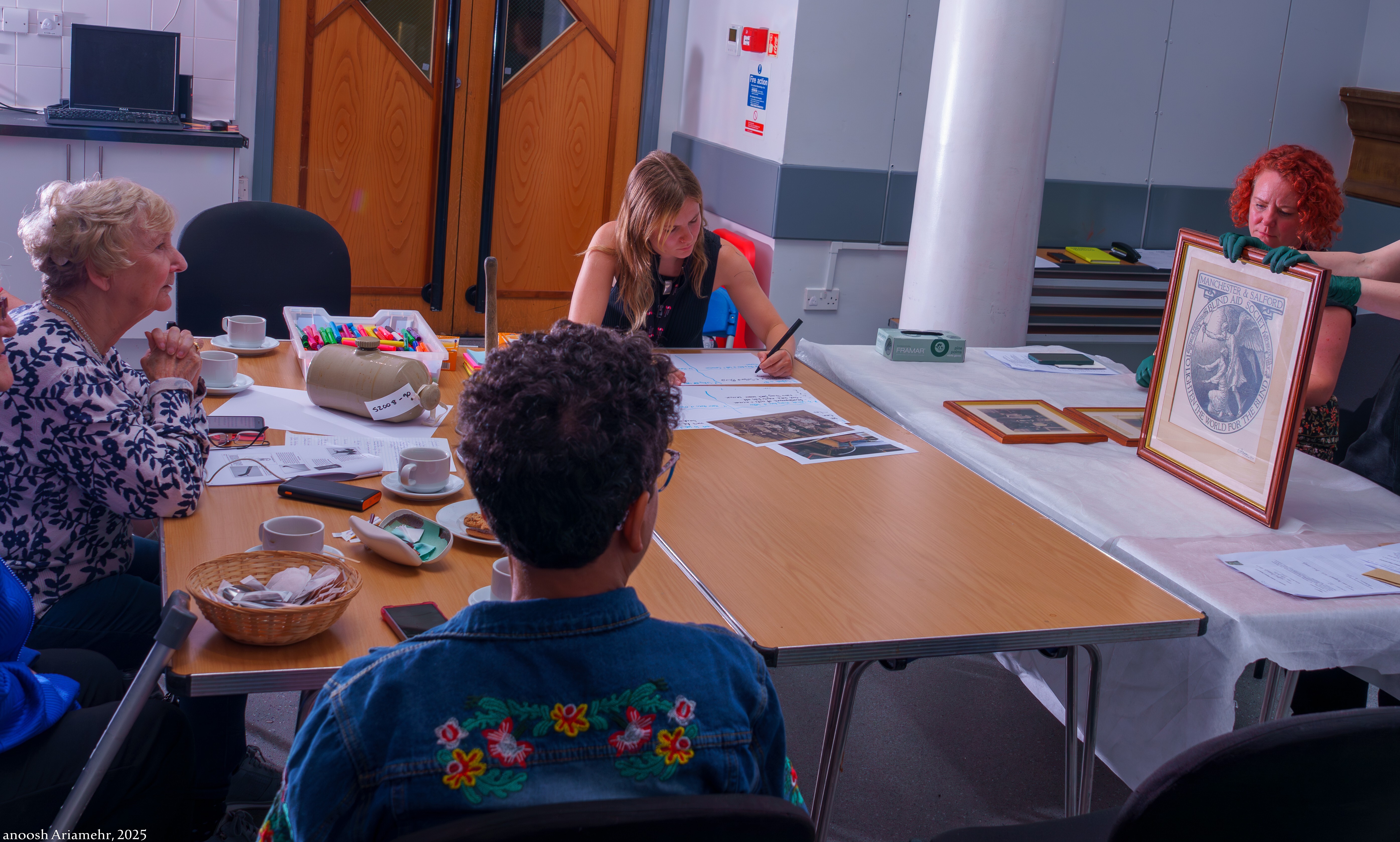A photograph of an arts and crafts event, three women are sat at a table with another women showing them a piece of art.