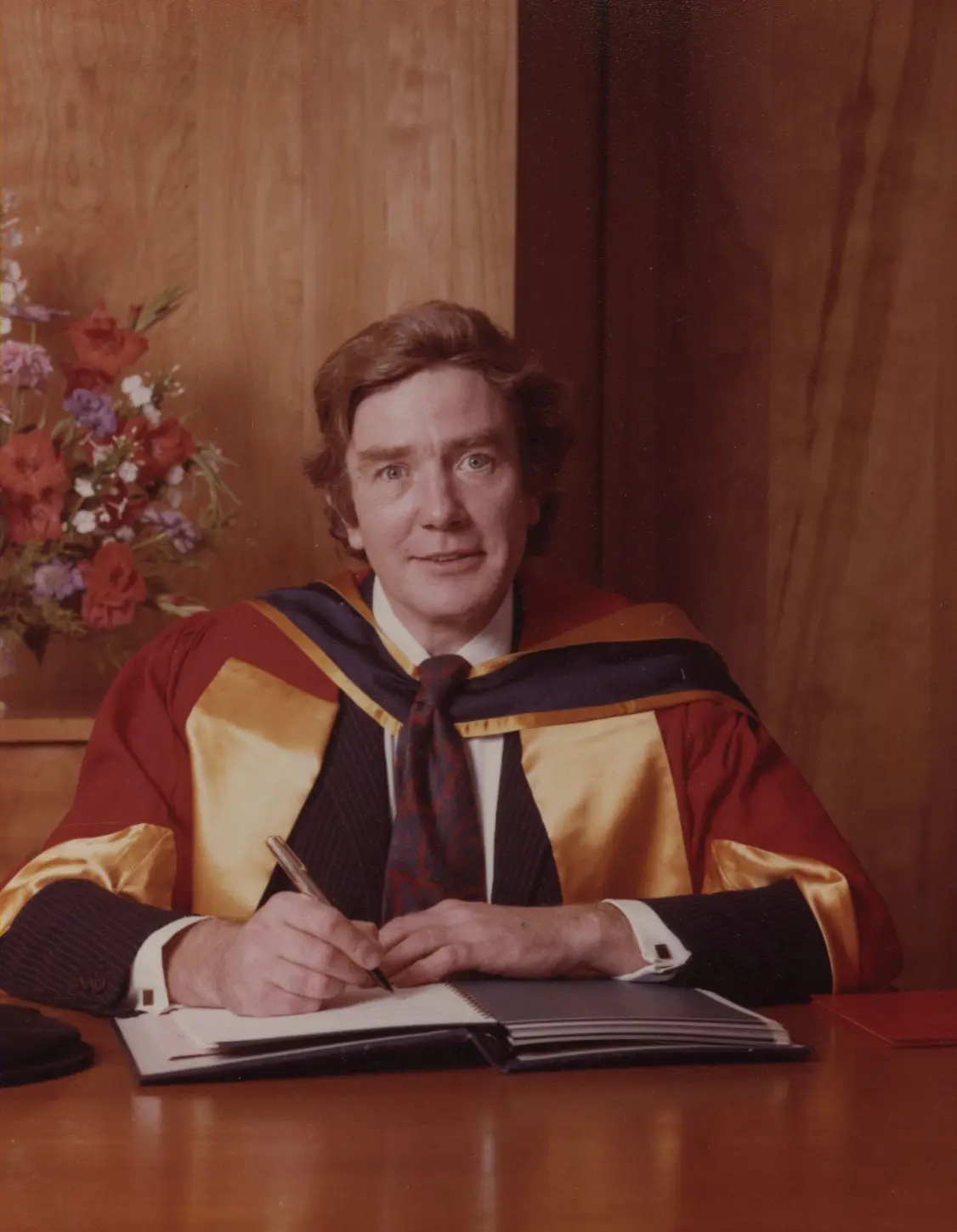 A photograph of Albert Finney, sat at a desk writing in a book.